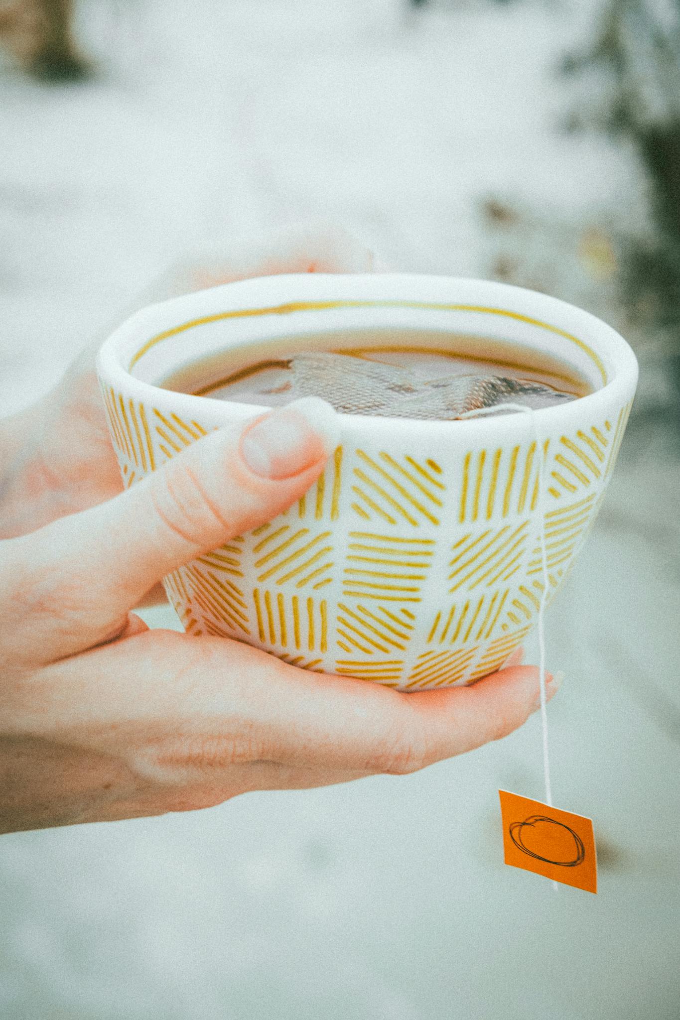 A warm cup of tea held in hands on a snowy winter day, perfect for cozy moments.