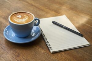 Freelancing Services available for writing health content. Cup of coffee with notepad and pen on wooden table. Freelancing Services available for writing health content. Cup of coffee with notepad and pen on wooden table.