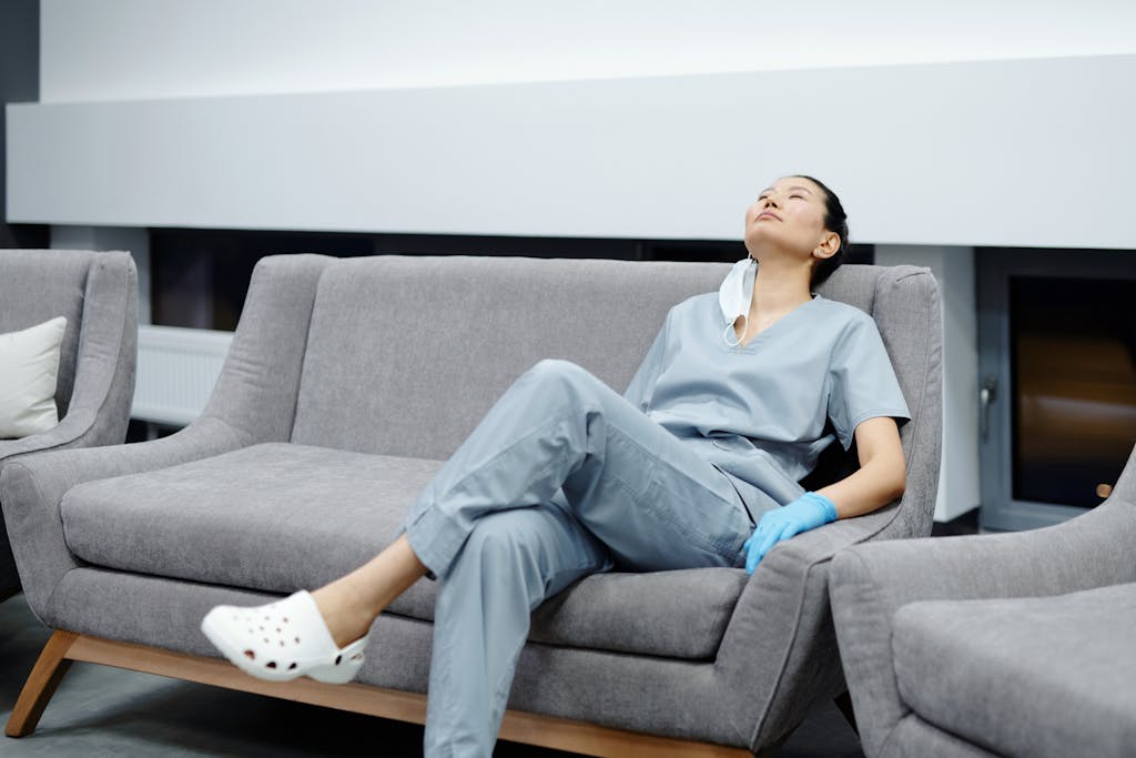 Nurse in scrubs takes a break, resting on a comfy hospital couch after a long shift feeling functional burnout