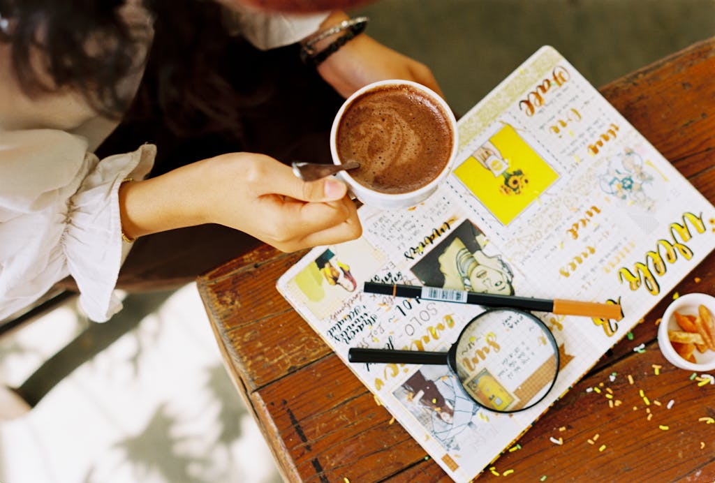Person enjoying hot coffee while writing in a creative journal for self care on a wooden table