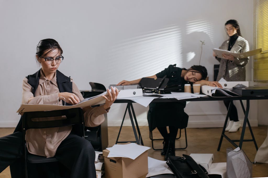 Three women, overwhelmed with paperwork in a cluttered office setting, stressed and stuck.