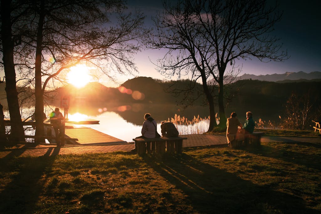 Tranquil scene of people relaxing by a lake during sunset at a scenic park, resting releasing chronic stress from survival mode