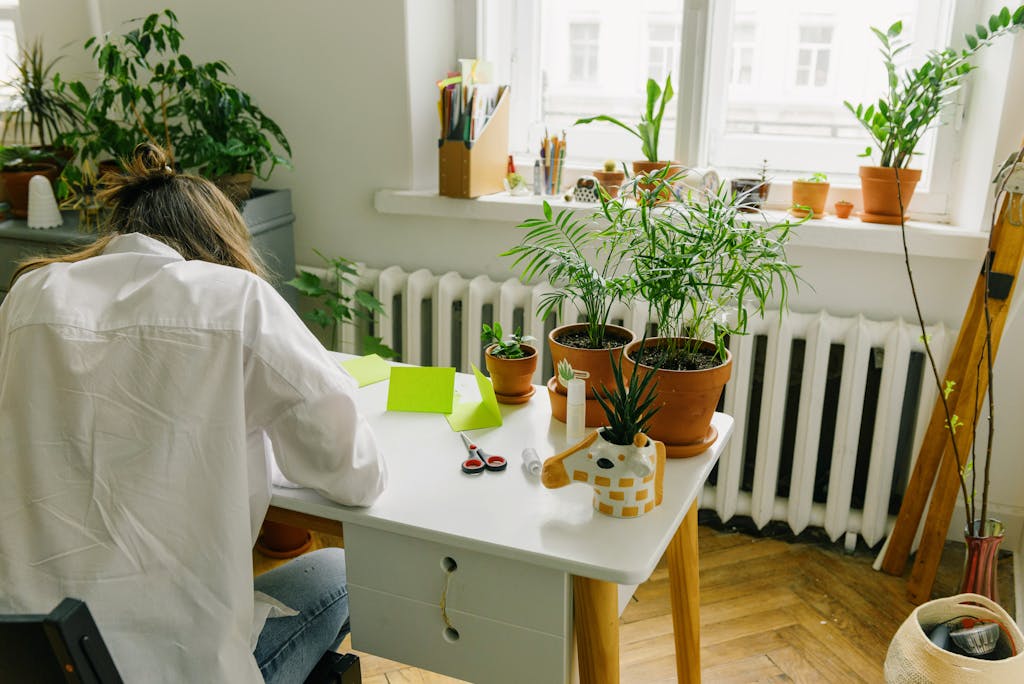 A woman in a cozy indoor workspace with potted plants and natural light.