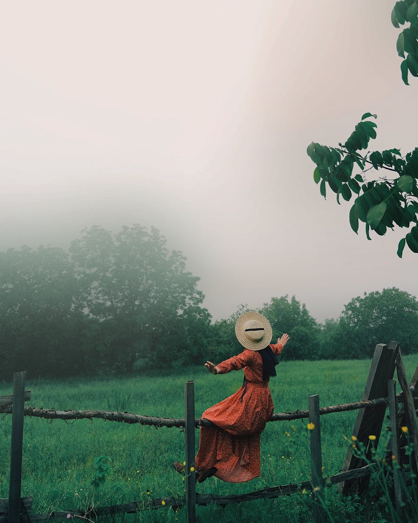 A woman in a red dress sitting on a wooden fence surrounded by greenery.
