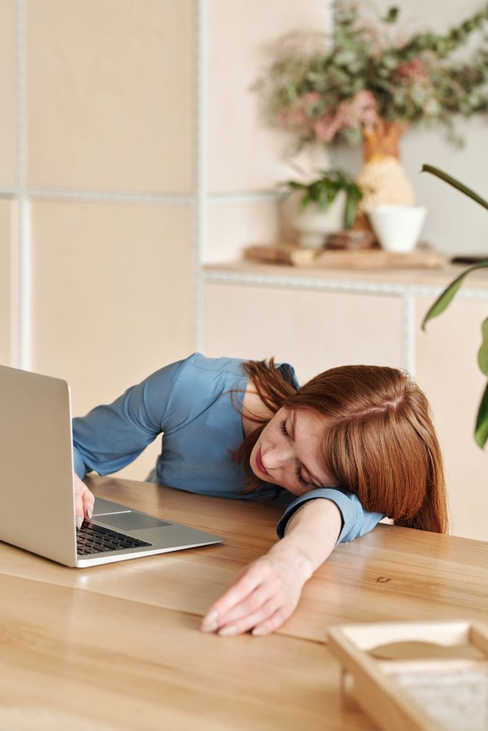 Woman in blue dress asleep from burnout and stress on desk with laptop nearby in a modern office.