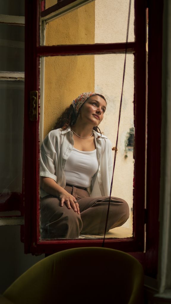 A woman in casual clothing sits relaxed on a window sill, embracing the calm atmosphere from a freeze response.